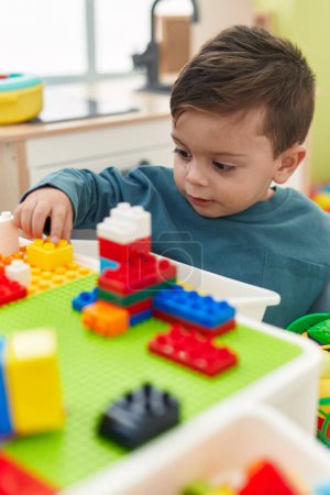 Foto de Adorable niño hispano jugando con bloques de construcción sentado en la mesa en el jardín de infantes - Imagen libre de derechos