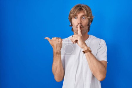 Téléchargez les photos : Middle age man standing over blue background asking to be quiet with finger on lips pointing with hand to the side. silence and secret concept. - en image libre de droit