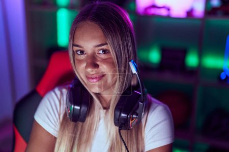 Photo for Young beautiful hispanic woman streamer smiling confident sitting on table at gaming room - Royalty Free Image