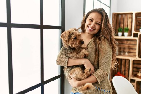 Photo for Young beautiful hispanic woman hugging dog standing at home - Royalty Free Image