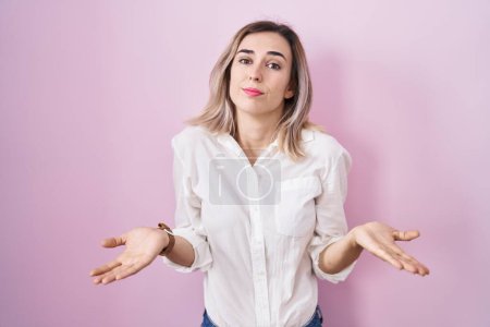 Photo for Young beautiful woman standing over pink background clueless and confused with open arms, no idea concept. - Royalty Free Image