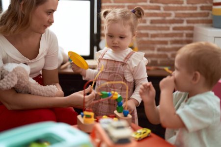 Foto de Profesor con niño y niña jugando con juguetes sentados en la mesa en el jardín de infantes - Imagen libre de derechos