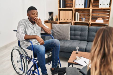 Téléchargez les photos : Afro-Américain faisant de la thérapie assis sur fauteuil roulant ennuyé bâillant fatigué couvrant la bouche avec la main. agitation et somnolence. - en image libre de droit