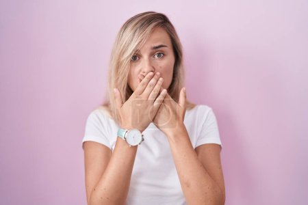 Photo for Young blonde woman standing over pink background shocked covering mouth with hands for mistake. secret concept. - Royalty Free Image