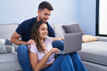 Photo for Young hispanic couple using laptop sitting on sofa at home - Royalty Free Image