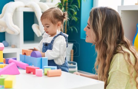 Photo for Teacher and toddler playing with geometry blocks sitting on table at kindergarten - Royalty Free Image