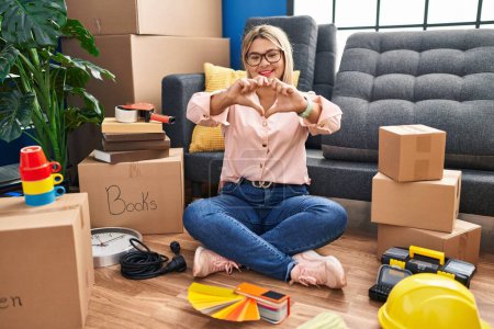 Photo for Young hispanic woman moving to a new home sitting on the floor smiling in love doing heart symbol shape with hands. romantic concept. - Royalty Free Image