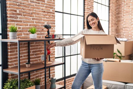 Photo for Young woman smiling confident unboxing fragile cardboard box at new home - Royalty Free Image