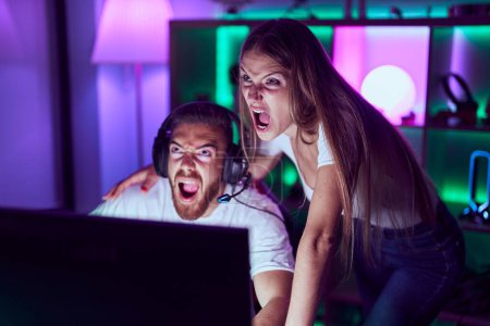 Photo for Young couple playing video games angry and mad screaming frustrated and furious, shouting with anger looking up. - Royalty Free Image
