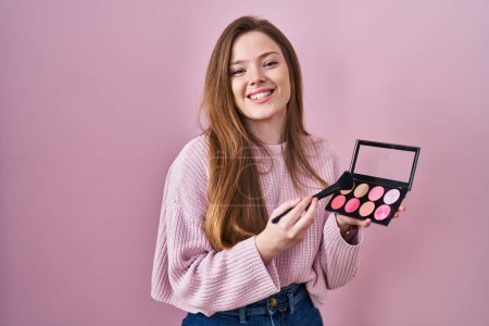Photo for Young caucasian woman holding makeup brush and blush palette smiling and laughing hard out loud because funny crazy joke. - Royalty Free Image