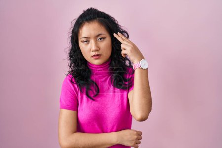 Photo for Young asian woman standing over pink background shooting and killing oneself pointing hand and fingers to head like gun, suicide gesture. - Royalty Free Image