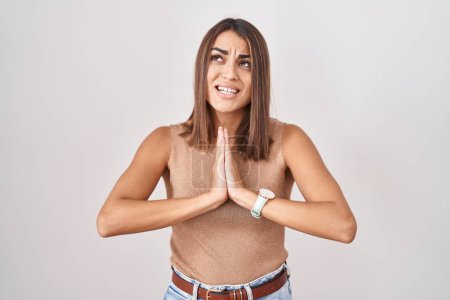 Téléchargez les photos : Young hispanic woman standing over white background begging and praying with hands together with hope expression on face very emotional and worried. begging. - en image libre de droit