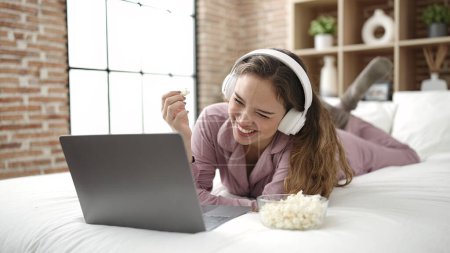 Téléchargez les photos : Young beautiful hispanic woman watching movie eating popcorn at bedroom - en image libre de droit