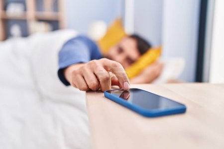 Foto de Joven hispano durmiendo en la cama apagando la alarma de smartphone en el dormitorio - Imagen libre de derechos