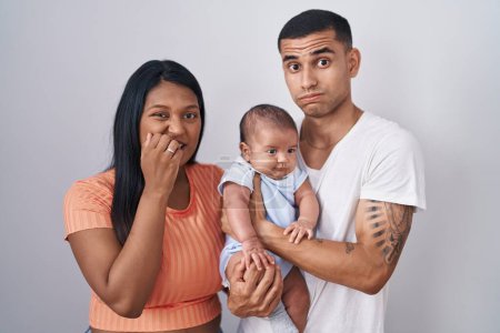Foto de Young hispanic couple with baby standing together over isolated background looking stressed and nervous with hands on mouth biting nails. anxiety problem. - Imagen libre de derechos