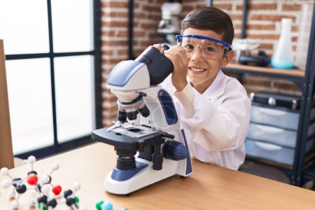 Foto de Adorable estudiante hispano sonriendo confiado usando microscopio en el aula de laboratorio - Imagen libre de derechos
