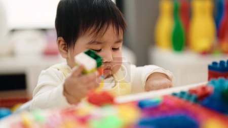 Photo for Adorable hispanic baby playing with construction blocks sitting on table at kindergarten - Royalty Free Image