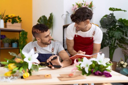 Téléchargez les photos : Two hispanic men florists cutting stem of flower writing on notebook at flower shop - en image libre de droit