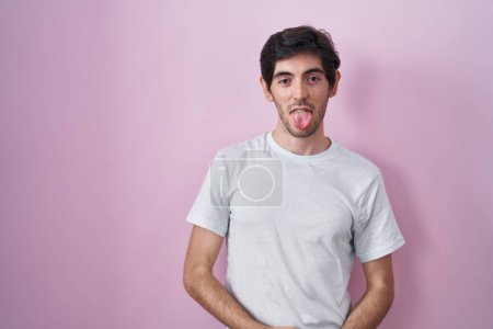Photo for Young hispanic man standing over pink background sticking tongue out happy with funny expression. emotion concept. - Royalty Free Image