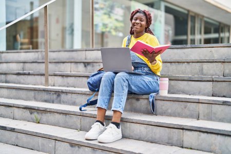 Téléchargez les photos : African american woman student using laptop reading book at university - en image libre de droit