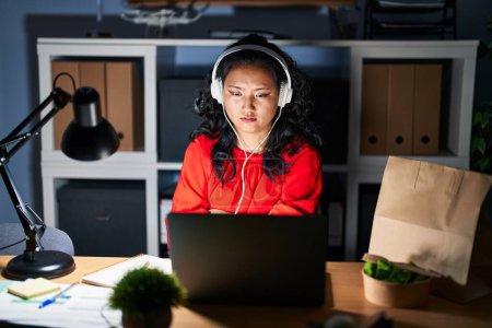 Téléchargez les photos : Jeune femme asiatique travaillant au bureau avec ordinateur portable la nuit sceptique et nerveuse, désapprouvant l'expression sur le visage avec les bras croisés. personne négative. - en image libre de droit