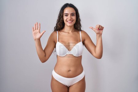 Téléchargez les photos : Jeune femme hispanique portant une lingerie blanche montrant et pointant vers le haut avec les doigts numéro six tout en souriant confiant et heureux. - en image libre de droit