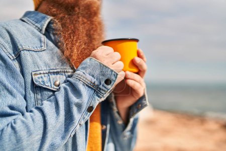 Téléchargez les photos : Jeune rousse homme buvant une tasse de café au bord de la mer - en image libre de droit