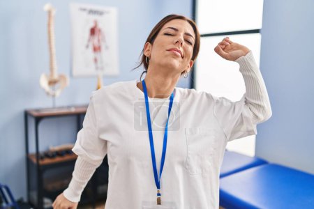 Foto de Young brunette woman working at pain recovery clinic stretching back, tired and relaxed, sleepy and yawning for early morning - Imagen libre de derechos