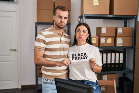 Photo for Young couple working at small business holding black friday banner puffing cheeks with funny face. mouth inflated with air, catching air. - Royalty Free Image