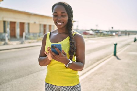 Téléchargez les photos : Femme afro-américaine portant des vêtements de sport à l'aide d'un smartphone dans la rue - en image libre de droit