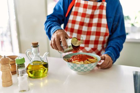 Photo for Senior man pouring tomato sauce on spaghetti at kitchen - Royalty Free Image
