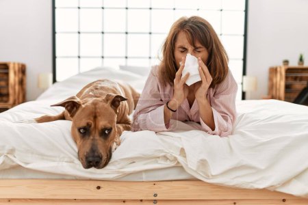 Téléchargez les photos : Jeune femme caucasienne maladie à l'aide de serviette couchée sur le lit avec chien dans la chambre - en image libre de droit
