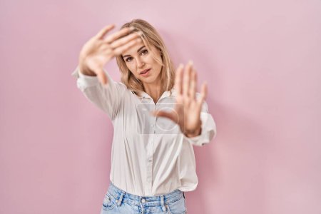 Photo for Young caucasian woman wearing casual white shirt over pink background doing frame using hands palms and fingers, camera perspective - Royalty Free Image