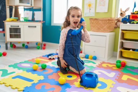 Photo for Adorable blonde girl playing with telephone toy sitting on floor at kindergarten - Royalty Free Image