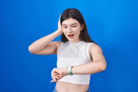 Téléchargez les photos : Jeune femme caucasienne debout sur fond bleu regardant le temps de la montre inquiet, peur d'arriver en retard - en image libre de droit