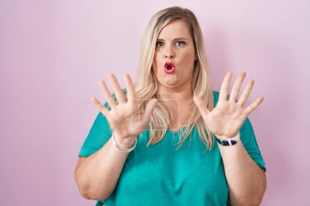 Foto de Caucasian plus size woman standing over pink background moving away hands palms showing refusal and denial with afraid and disgusting expression. stop and forbidden. - Imagen libre de derechos