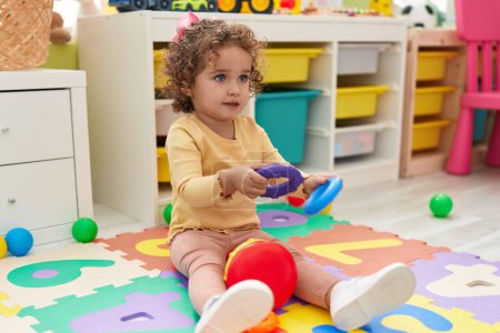 Photo for Adorable hispanic toddler playing with hoops toy sitting on floor at kindergarten - Royalty Free Image