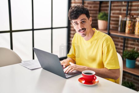Téléchargez les photos : Jeune homme caucasien utilisant ordinateur portable boire du café à la maison - en image libre de droit