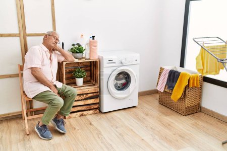 Photo for Senior man waiting for washing machine sleeping on chair at laundry room - Royalty Free Image