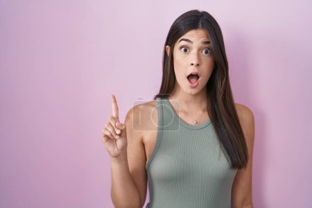 Photo for Hispanic woman standing over pink background pointing finger up with successful idea. exited and happy. number one. - Royalty Free Image