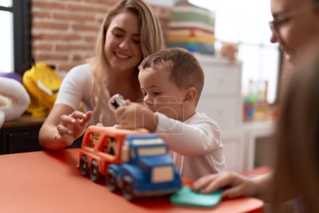 Téléchargez les photos : Professeurs avec garçon et fille jouant avec des voitures jouet assis sur la table à la maternelle - en image libre de droit