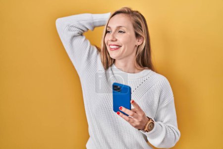 Photo for Young blonde woman using smartphone typing message smiling confident touching hair with hand up gesture, posing attractive and fashionable - Royalty Free Image