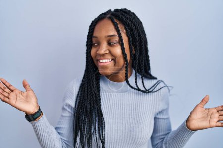 Téléchargez les photos : Femme afro-américaine debout sur fond bleu souriant montrant les paumes ouvertes des deux mains, présentant et comparant la publicité et l'équilibre - en image libre de droit