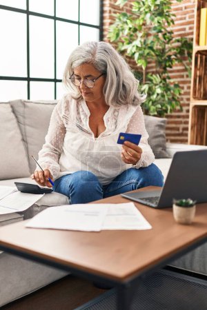 Foto de Mujer de mediana edad usando portátil y tarjeta de crédito en casa - Imagen libre de derechos