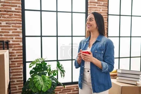 Téléchargez les photos : Young beautiful hispanic woman smiling confident drinking coffee at new home - en image libre de droit