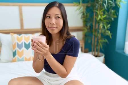 Photo for Young asian woman drinking cup of coffee sitting on bed at bedroom - Royalty Free Image