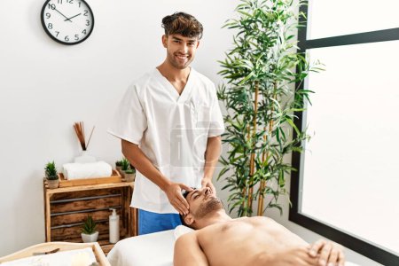 Photo for Two hispanic men therapist and patient having facial massage at beauty center - Royalty Free Image