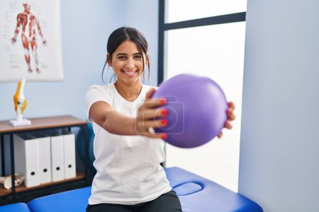 Photo for Young latin woman patient having rehab session using ball at physiotherapy clinic - Royalty Free Image