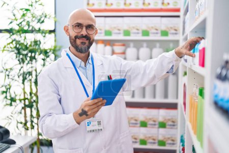 Téléchargez les photos : Young bald man pharmacist using touchpad holding medicine at pharmacy - en image libre de droit