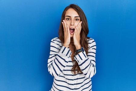 Photo for Young hispanic woman standing over blue isolated background afraid and shocked, surprise and amazed expression with hands on face - Royalty Free Image